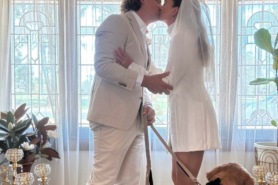 bride and groom kiss in front of a leadlight window while their dog looks on